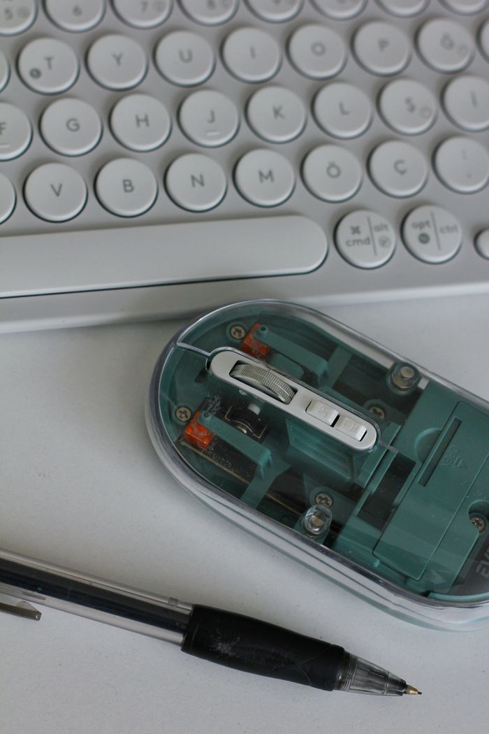 A top-down view of a keyboard, transparent mouse, and pen on a white desk, showcasing modern office essentials.