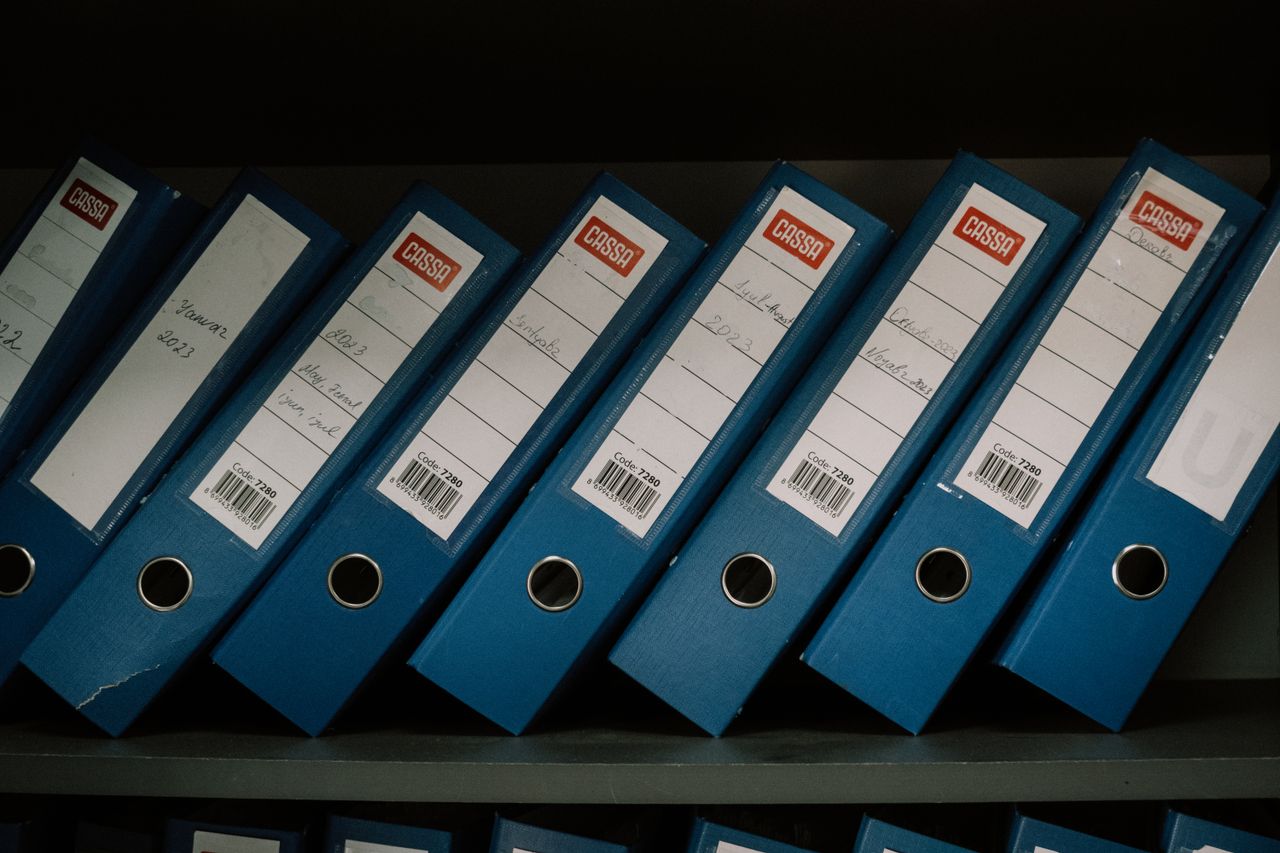 who-we-are Neatly arranged blue office binders labeled with dates and names for organized storage.