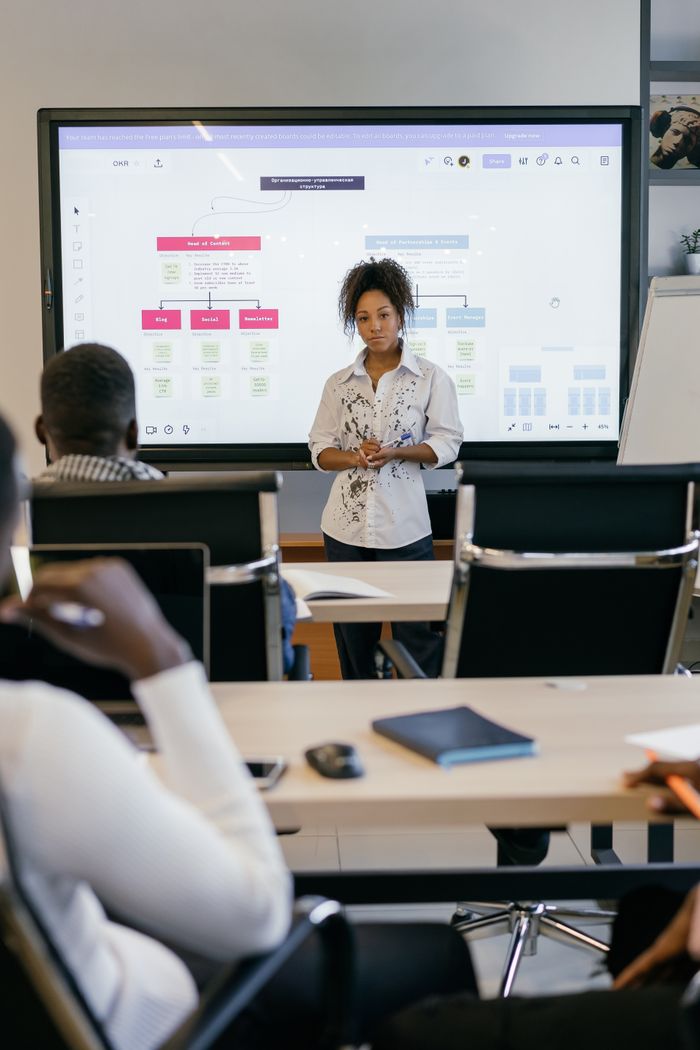 services-hero A professional business woman leads a meeting with a diverse team, using a digital display.